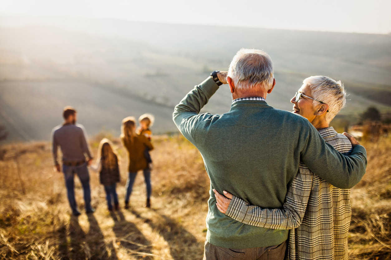 Back view of embraced grandparents enjoying while looking at their family on a hill in autumn day.